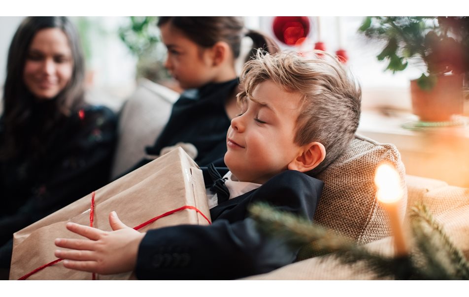 Pojken ler medan han håller en julklapp medan han sitter med familjen i vardagsrummet.