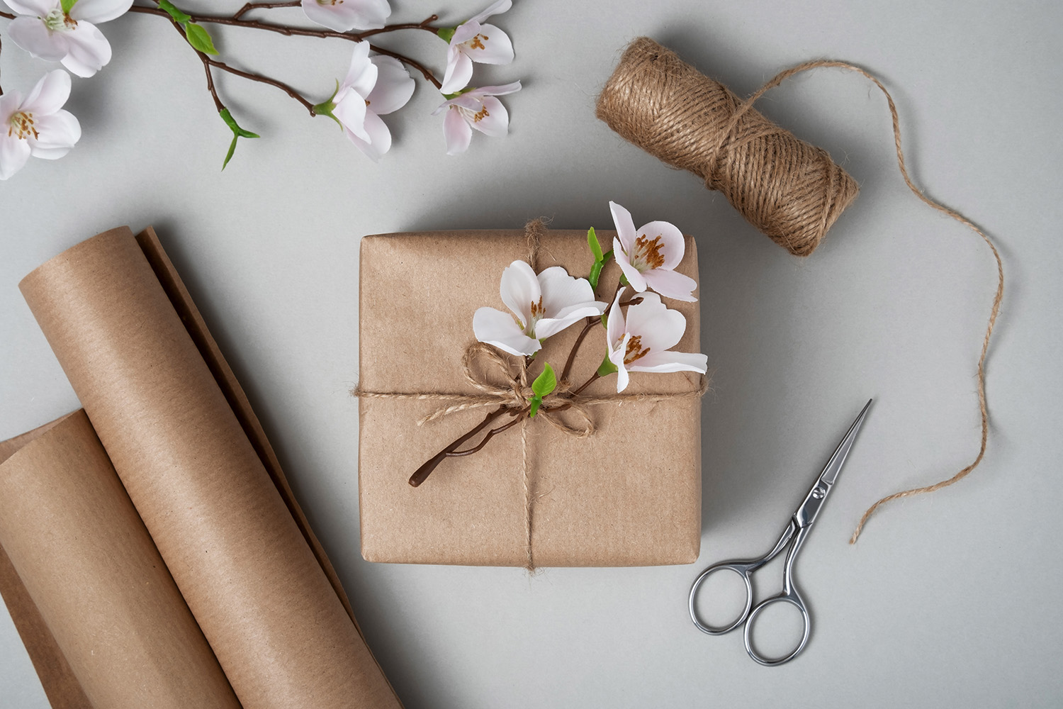 Ett presentpaket med blommor och brunt papper, sax och snöre på ljus bakgrund