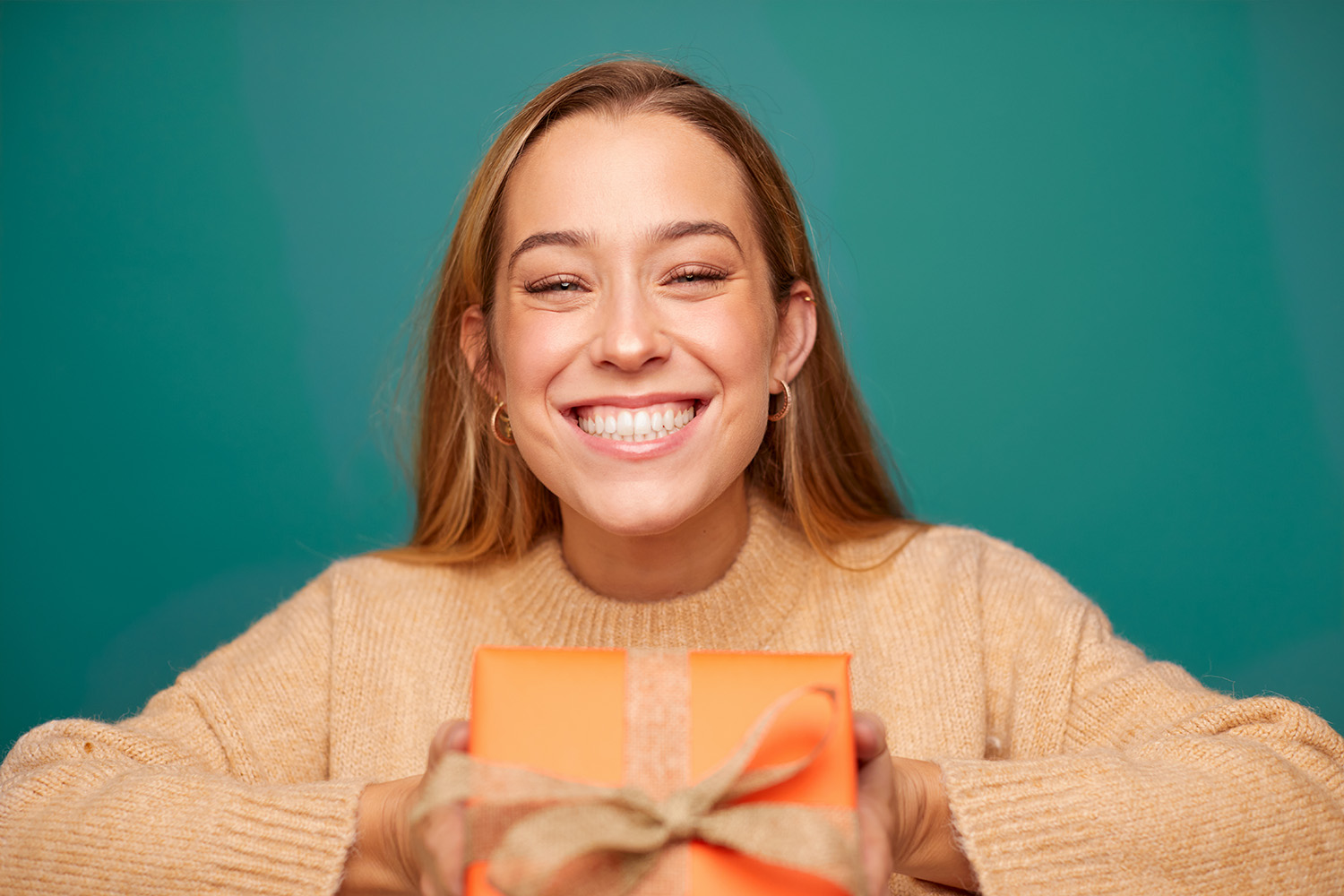 leende flicka med orange tröja som håller en orange presentförpackning