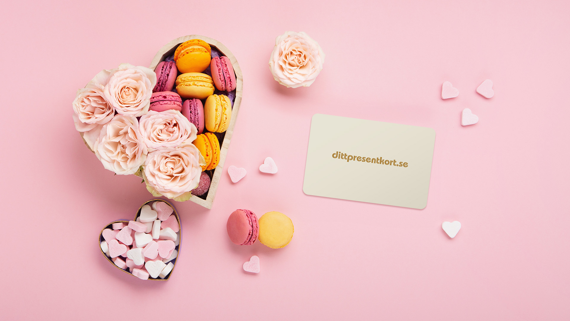 Dittpresentkort med hjärtformad ask med makroner och rosor och hjärtformade godis på rosa bakgrund